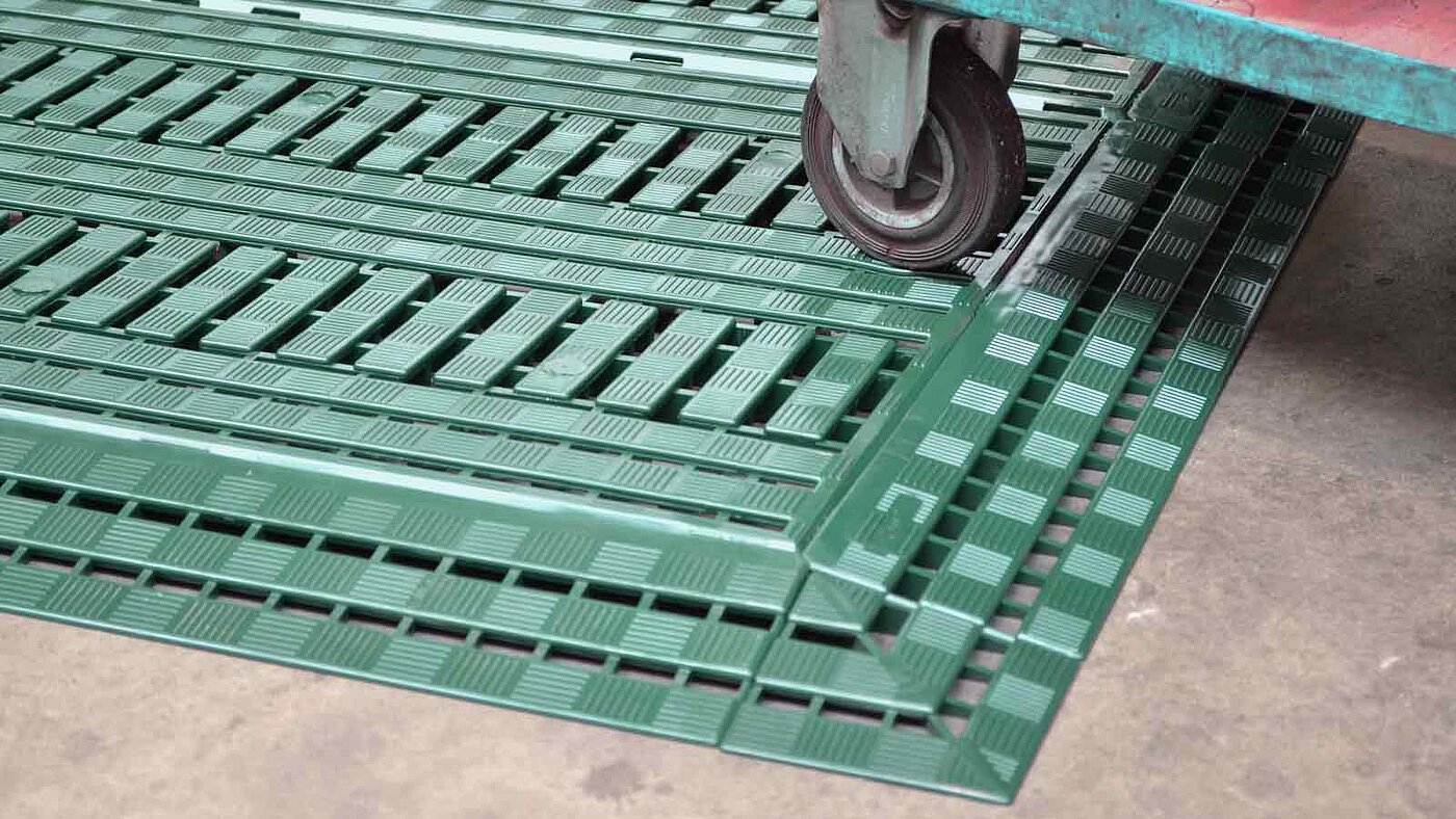 1 green floor-grating, made of plastics, with ramp pieces and corner piece, onto which a transport trolley is rolled