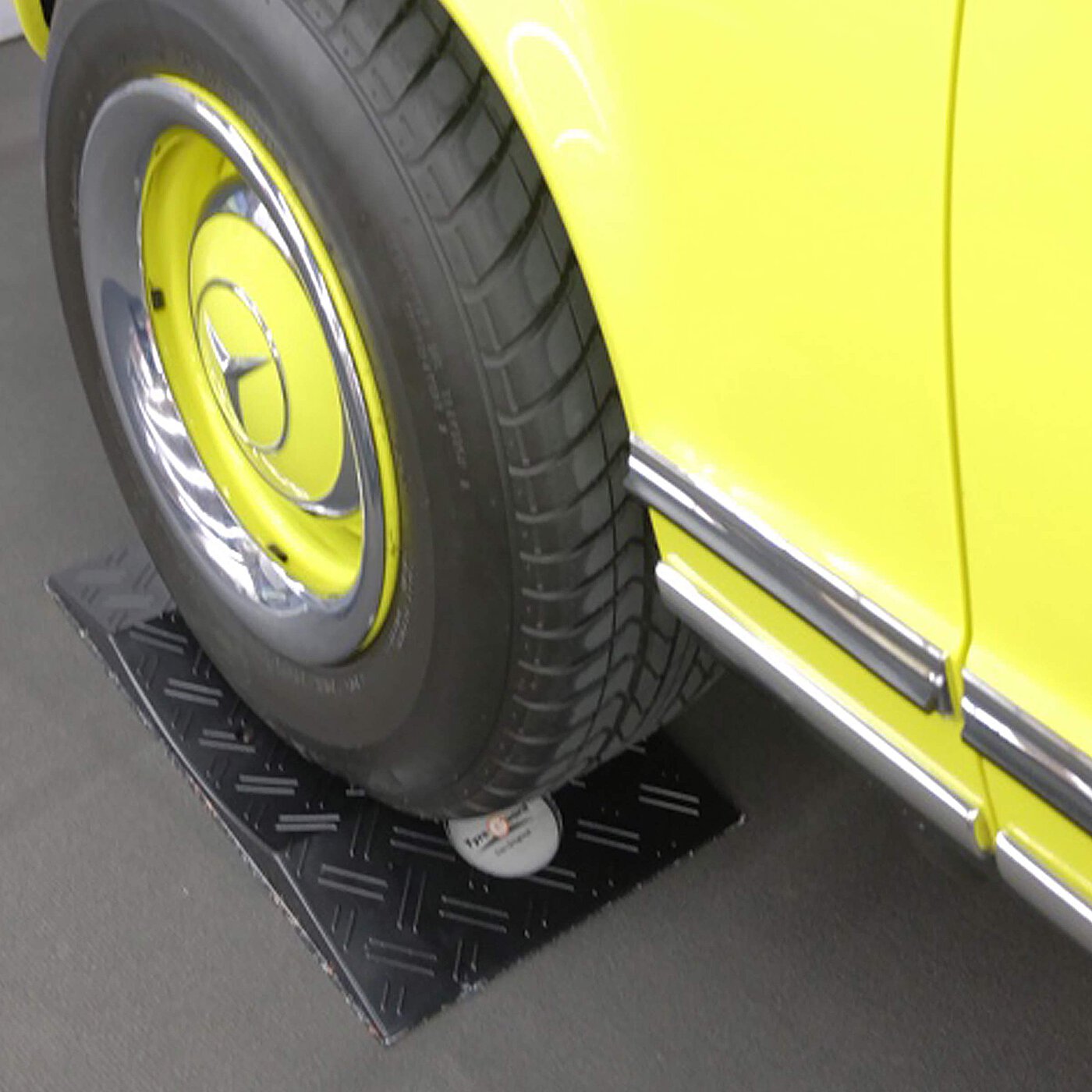 a black concave-shaped TyreGuard® tyre protector made of high-strength plastics, underneath a yellow youngtimer car