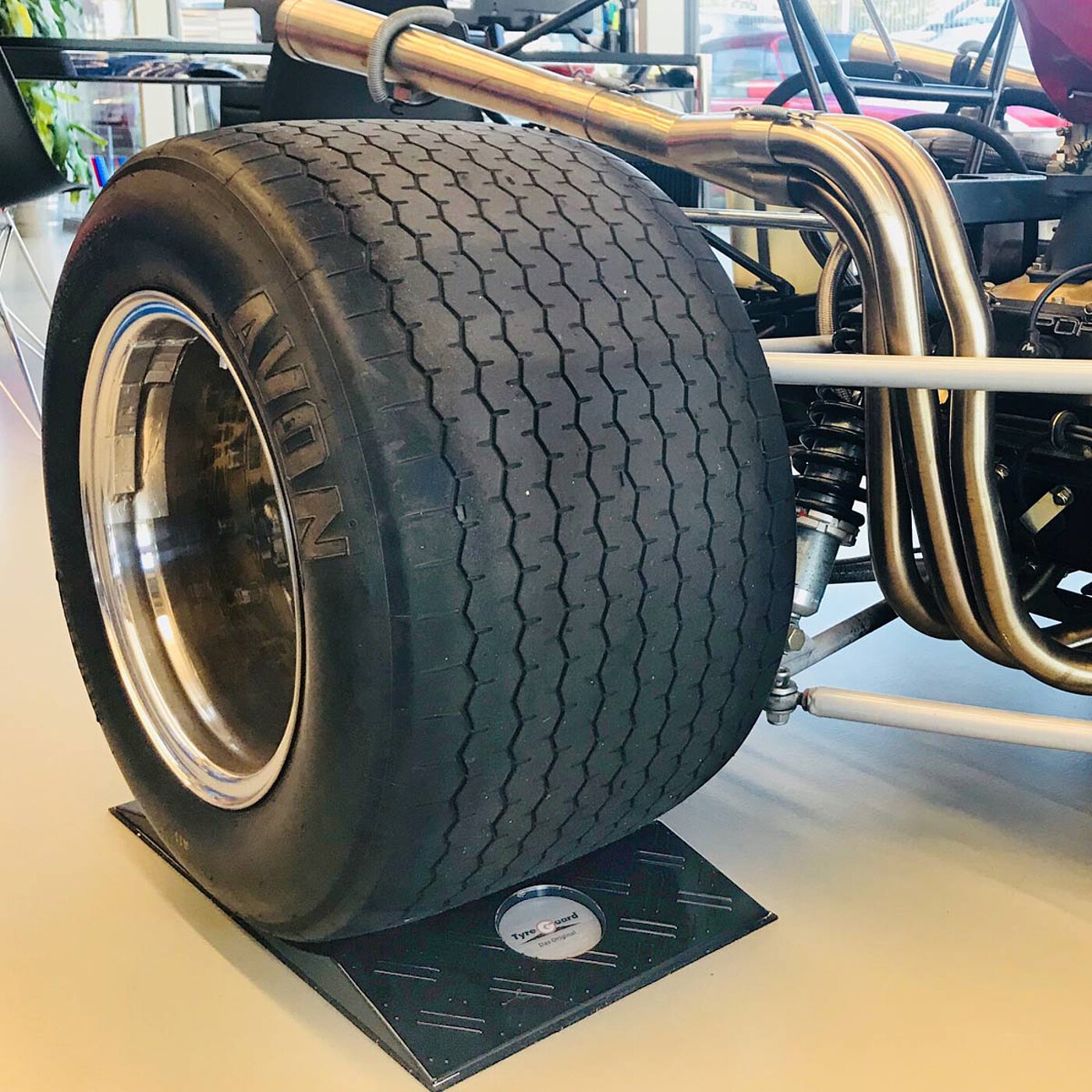 a black concave-shaped TyreGuard® tyre protector made of high-strength plastics, underneath a hot-rod car with openly ducted side exhaust pipe and very broad tyres