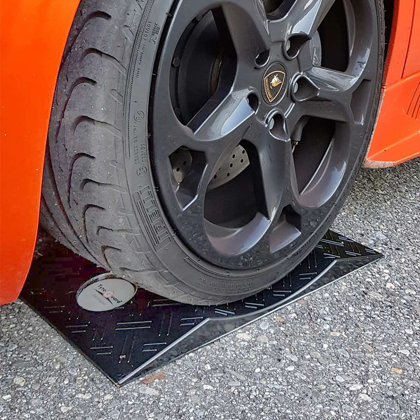 a black concave-shaped TyreGuard® tyre protector made of high-strength plastics and with anti-slip mat, underneath an orange-coloured modern high-performance sports car